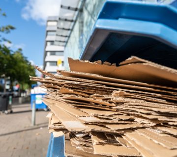 Used flattened cardboard boxes waiting to be collected in a blue plastic container for paper waste separation and recycling.